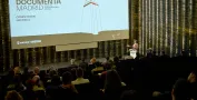 Sala de proyección de cine. Hombre habla desde atril señalando la pantalla
